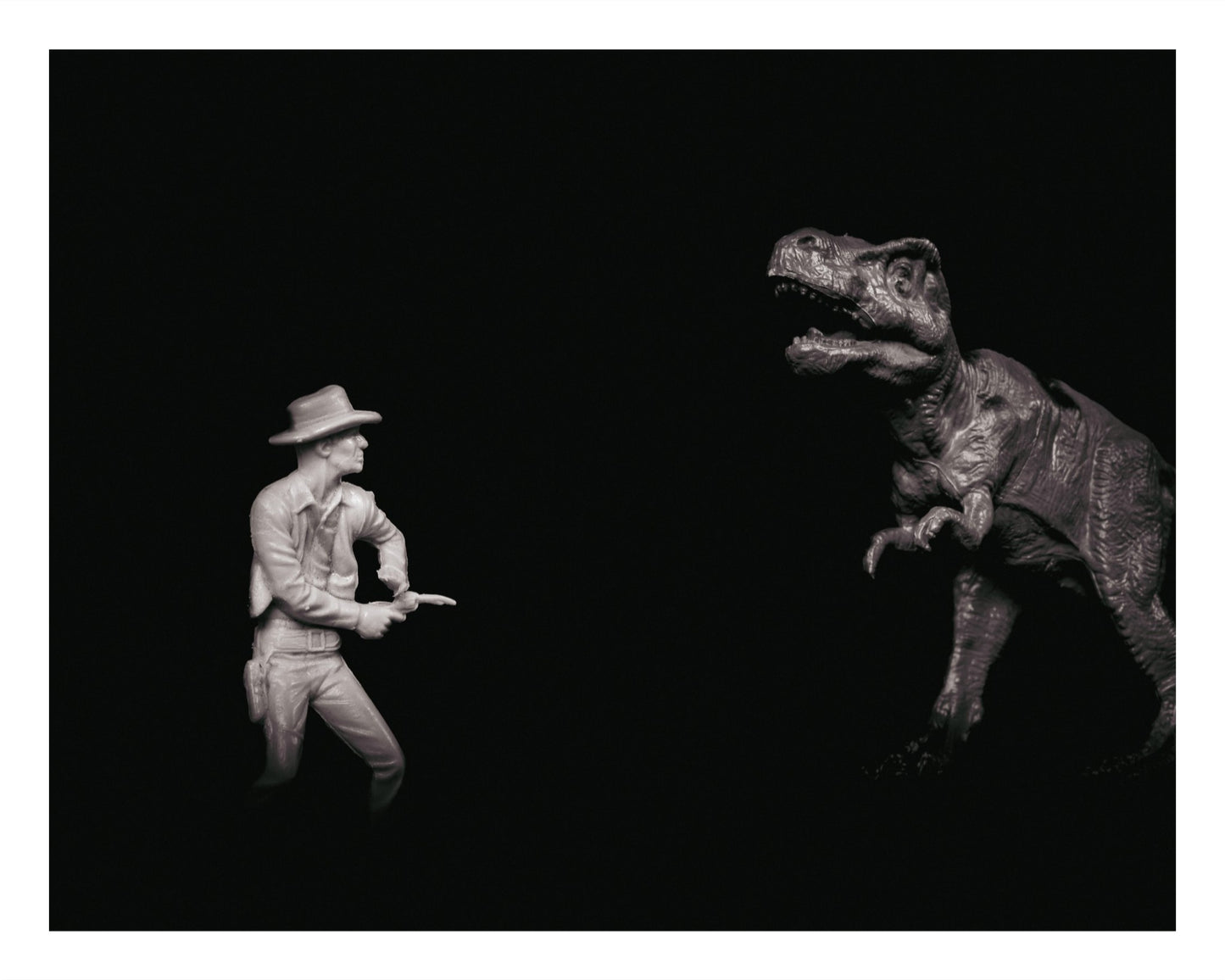 Black and white photo of a toy cowboy and a toy T. rex facing each other dramatically.