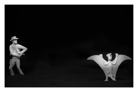 Toy cowboy pointing a gun at a toy Pteranodon with wings raised in surrender.