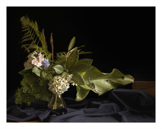 Color photograph of a floral arrangement with a brontosaurus and T. rex toy nestled among the flowers and foliage.