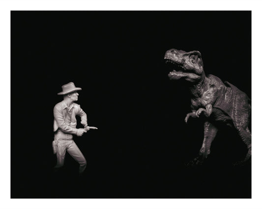 Black and white photo of a toy cowboy and a toy T. rex facing each other dramatically.